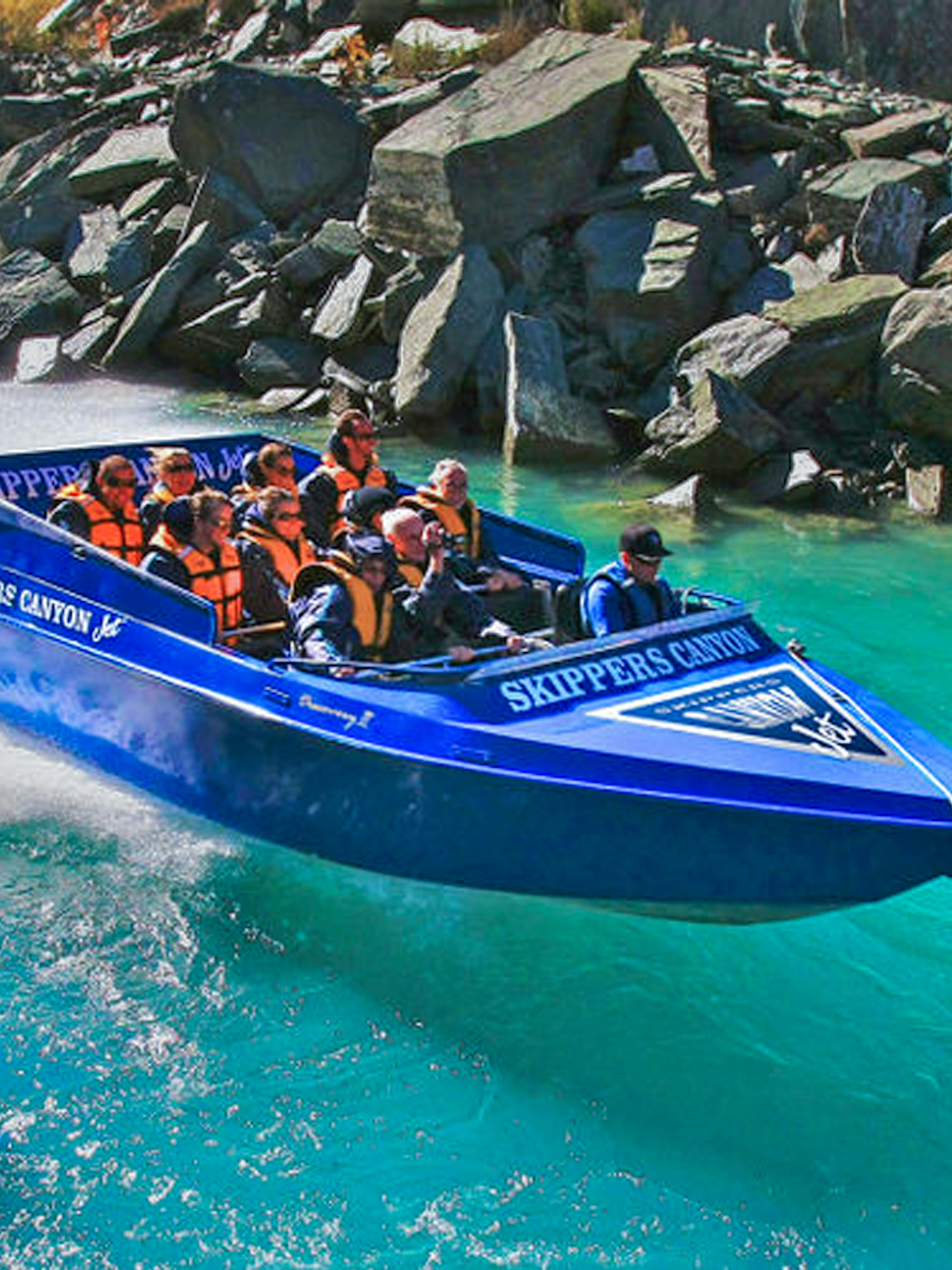 Tourists enjoying Skippers Canyon Jet Boat ride on turquoise river.