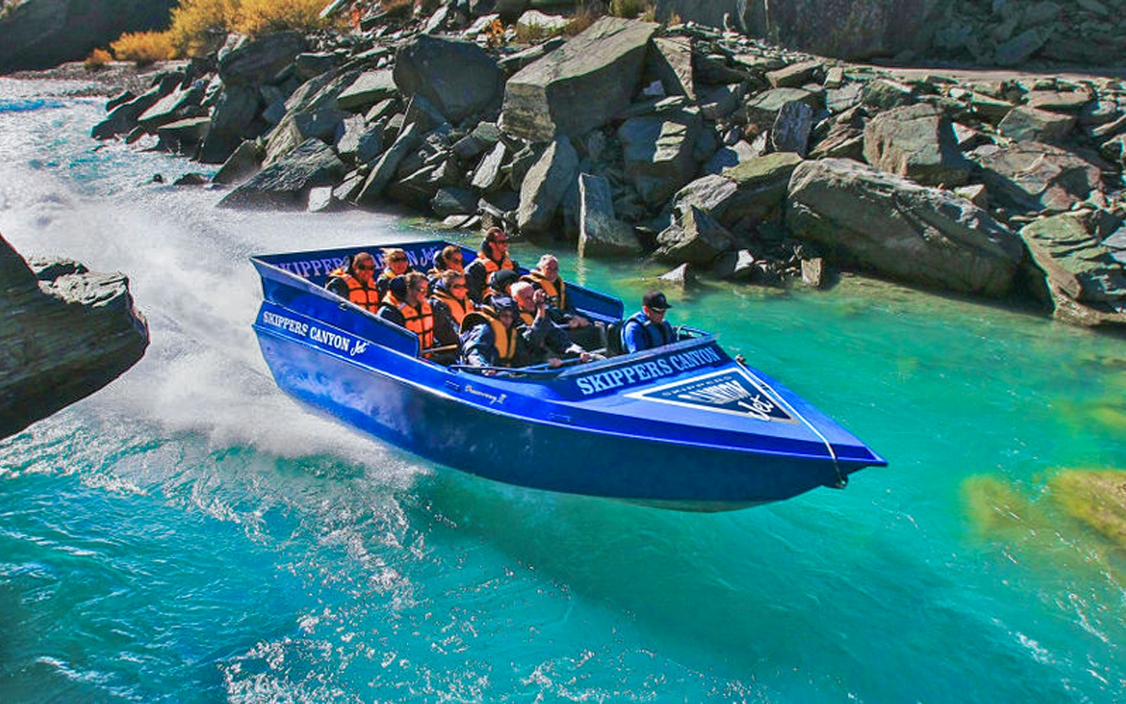 Tourists enjoying Skippers Canyon Jet Boat ride on turquoise river.