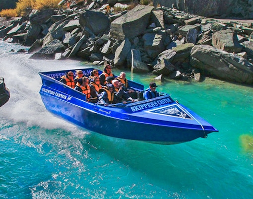 Tourists enjoying Skippers Canyon Jet Boat ride on turquoise river.