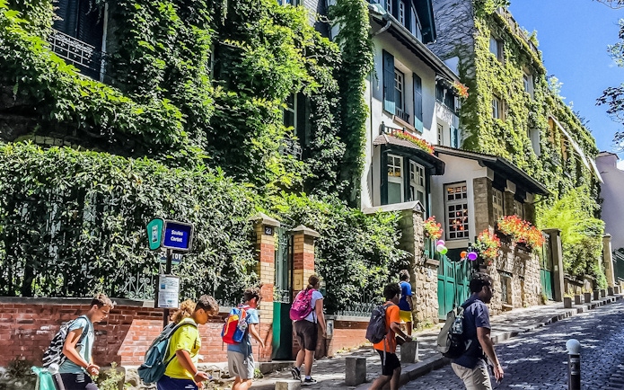 Tourists walking past ivy-covered buildings on Montmartre street, Paris.