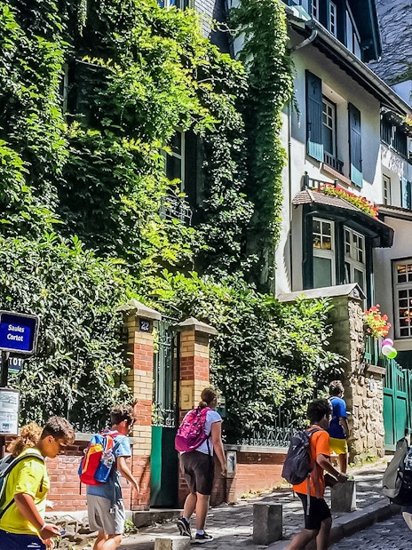Tourists walking past ivy-covered buildings on Montmartre street, Paris.