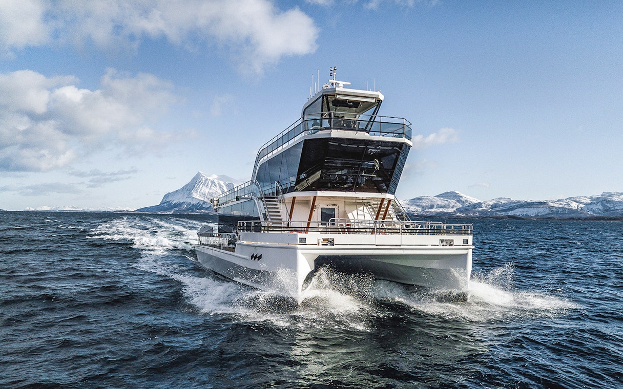Silent whale watching boat in Tromso fjord with snowy mountains in the background.