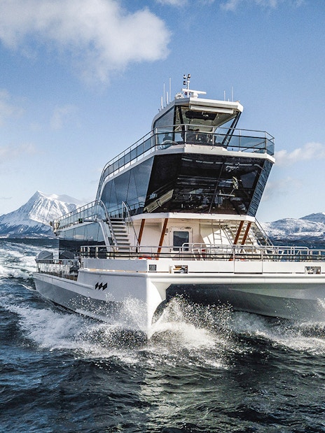 Silent whale watching boat in Tromso fjord with snowy mountains in the background.