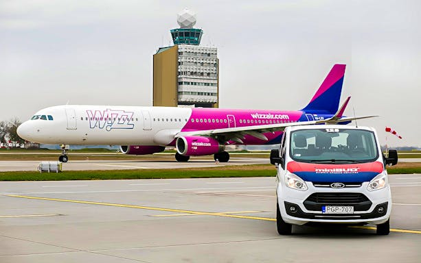 MiniBud Airport shuttle in front of Wizz Air plane at airport.