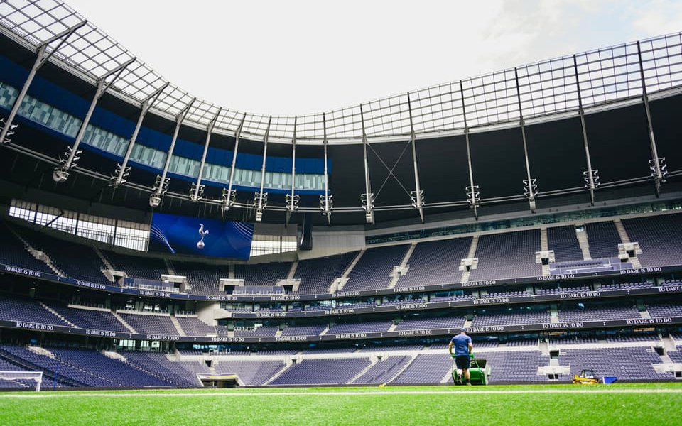 Groundskeeper maintaining the field at a modern stadium with empty seating.
