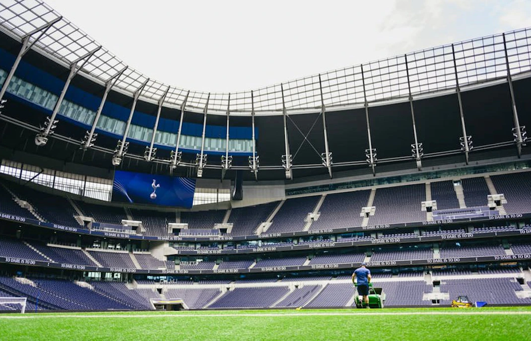 Groundskeeper maintaining the field at a modern stadium with empty seating.
