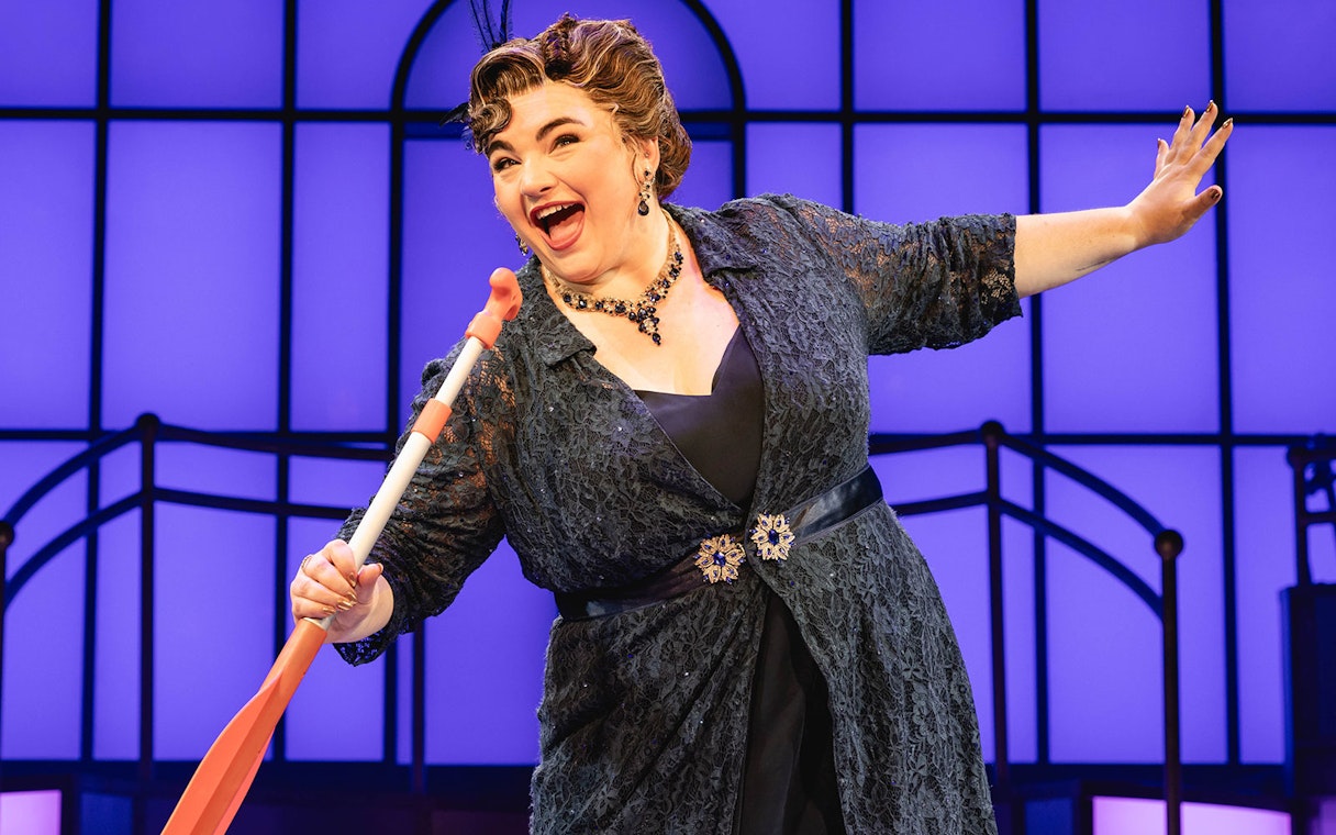 Performer on stage during Titanique West End show holding a prop against a blue backdrop.