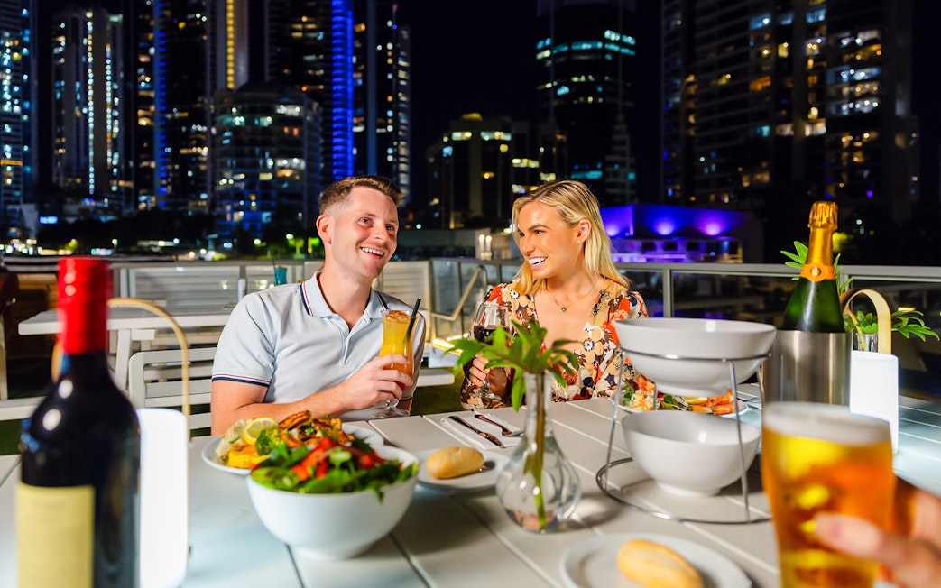 Couple dining on a Gold Coast sightseeing cruise with city skyline in the background.