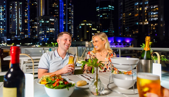 Couple dining on a Gold Coast sightseeing cruise with city skyline in the background.
