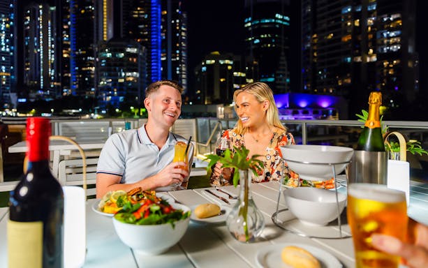 Couple dining on a Gold Coast sightseeing cruise with city skyline in the background.