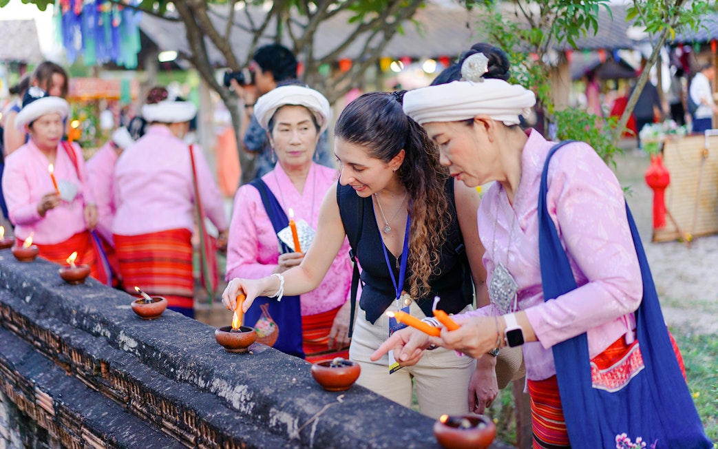 Visitor lighting clay lamps with local women in pink attire during Yi Peng and Loy Krathong Festival 2025, Chiang Mai.