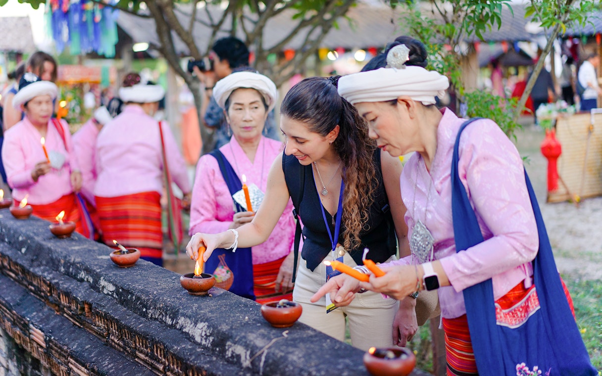 Visitor lighting clay lamps with local women in pink attire during Yi Peng and Loy Krathong Festival 2025, Chiang Mai.