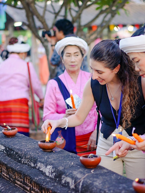 Visitor lighting clay lamps with local women in pink attire during Yi Peng and Loy Krathong Festival 2025, Chiang Mai.