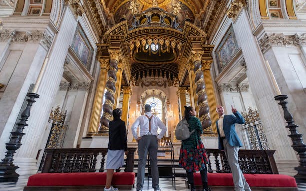 Visitors inside St Paul's Cathedral, London, admiring ornate columns and stained glass.