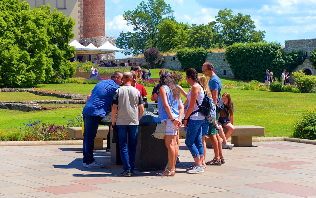 Tourists examining a miniature model of Wawel Royal Castle in a garden setting.