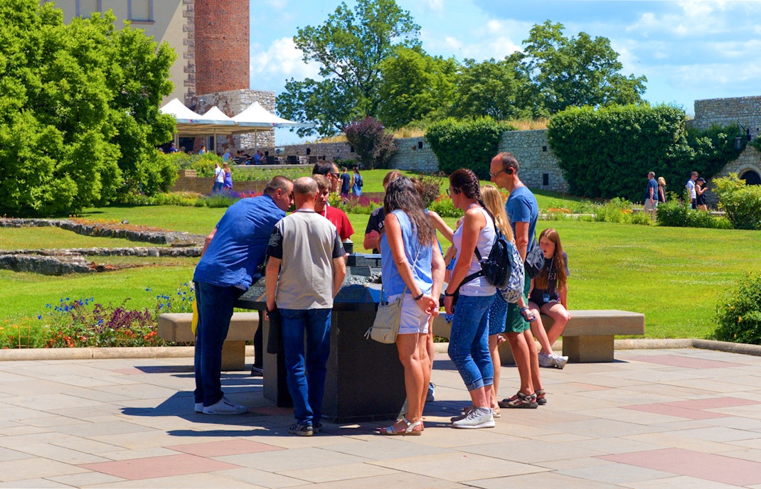 Tourists examining a miniature model of Wawel Royal Castle in a garden setting.