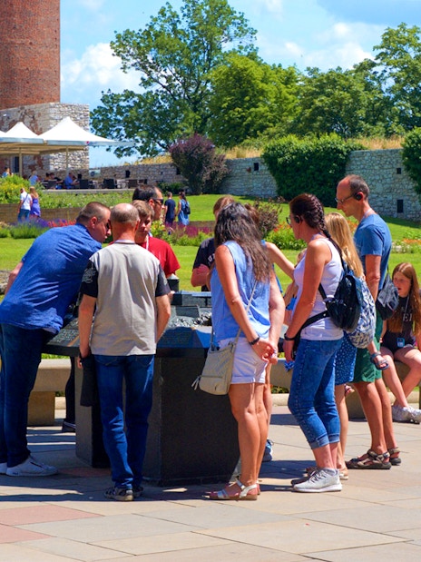 Tourists examining a miniature model of Wawel Royal Castle in a garden setting.