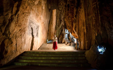 Person exploring illuminated cave with statue, Marble Mountains, Da Nang, Vietnam.