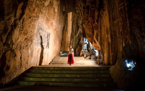 Person exploring illuminated cave with statue, Marble Mountains, Da Nang, Vietnam.