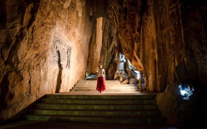 Person exploring illuminated cave with statue, Marble Mountains, Da Nang, Vietnam.
