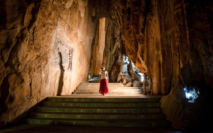 Person exploring illuminated cave with statue, Marble Mountains, Da Nang, Vietnam.