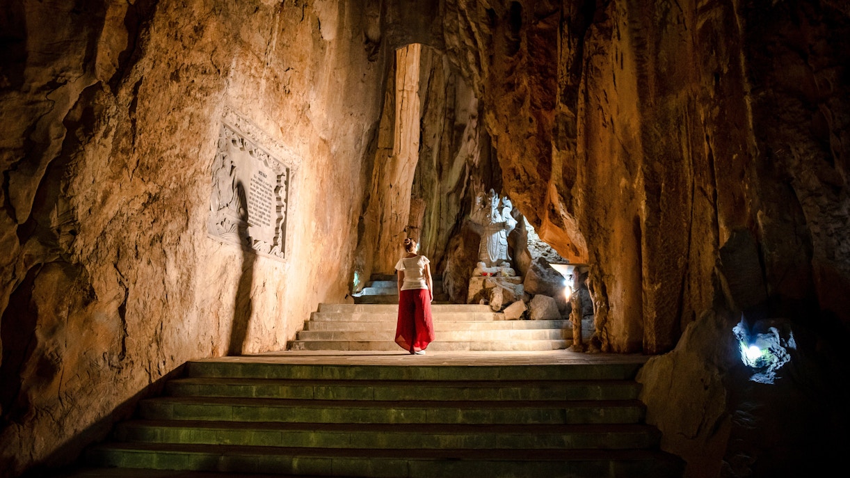 Person exploring illuminated cave with statue, Marble Mountains, Da Nang, Vietnam.