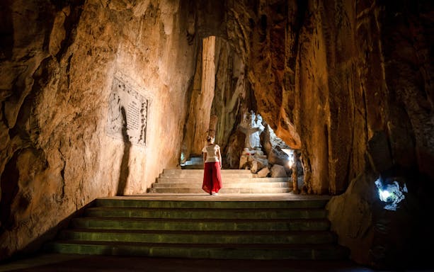 Person exploring illuminated cave with statue, Marble Mountains, Da Nang, Vietnam.