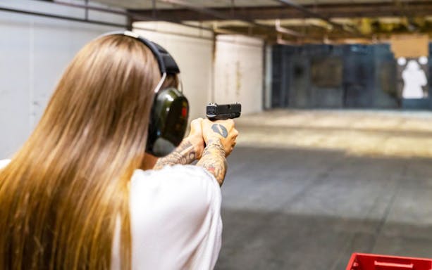 Person aiming a handgun at a target in an indoor shooting range.