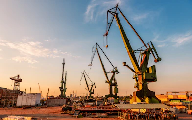 Gdansk port cranes silhouetted against a sunset sky.