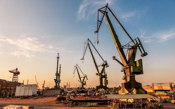 Gdansk port cranes silhouetted against a sunset sky.