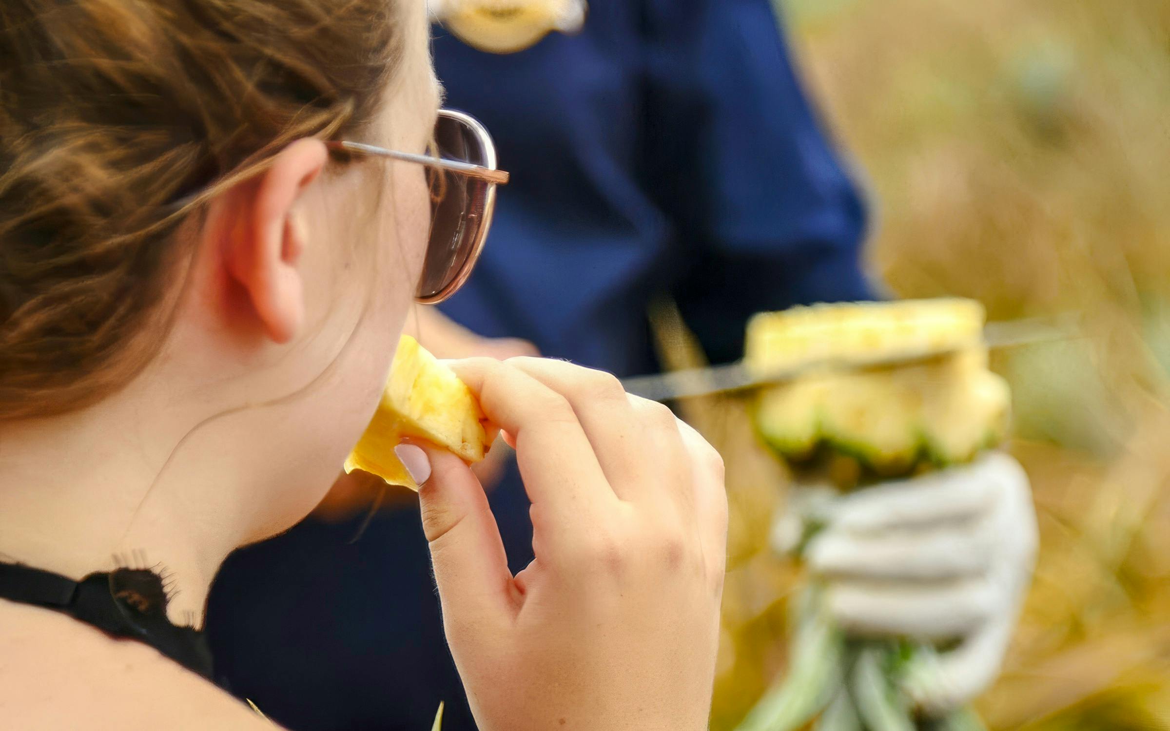 Person tasting fresh pineapple at a plantation tour.