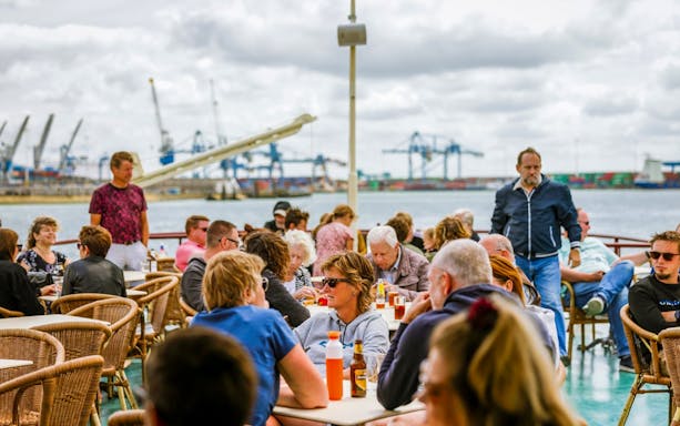 Guests enjoying the view on the deck of Rotterdam Historical Cruise with port cranes in background.