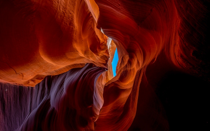 Red sandstone formations in Deer Canyon, Arizona with a view of the sky through a narrow opening.