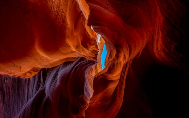 Red sandstone formations in Deer Canyon, Arizona with a view of the sky through a narrow opening.