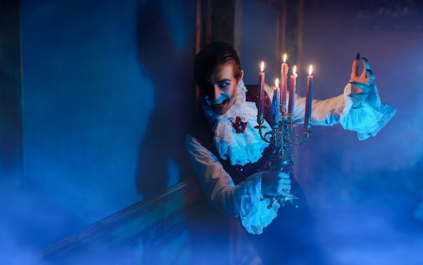 Person in vampire costume holding candelabra at Dracula's Castle Halloween tour.