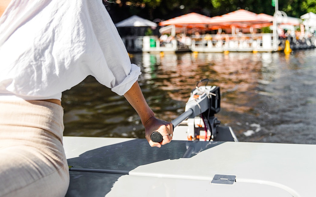 Person steering a boat on Yarra River during a self-drive picnic cruise.