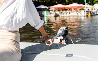 Person steering a boat on Yarra River during a self-drive picnic cruise.