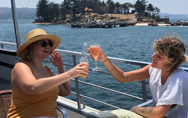 Guests enjoying drinks on a Sydney Harbour luxury dinner cruise with scenic island view.