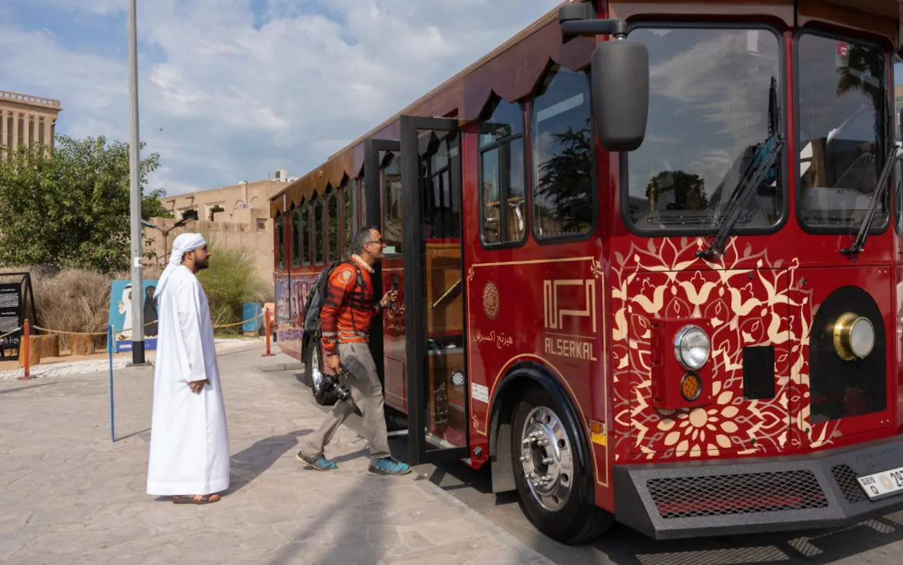 Man boarding Emirati trolley at Dubai heritage site for cultural tour.