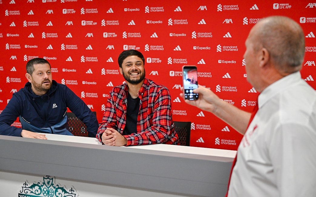 Guests in the press room at Anfield, with one taking a photo of two others at a table.