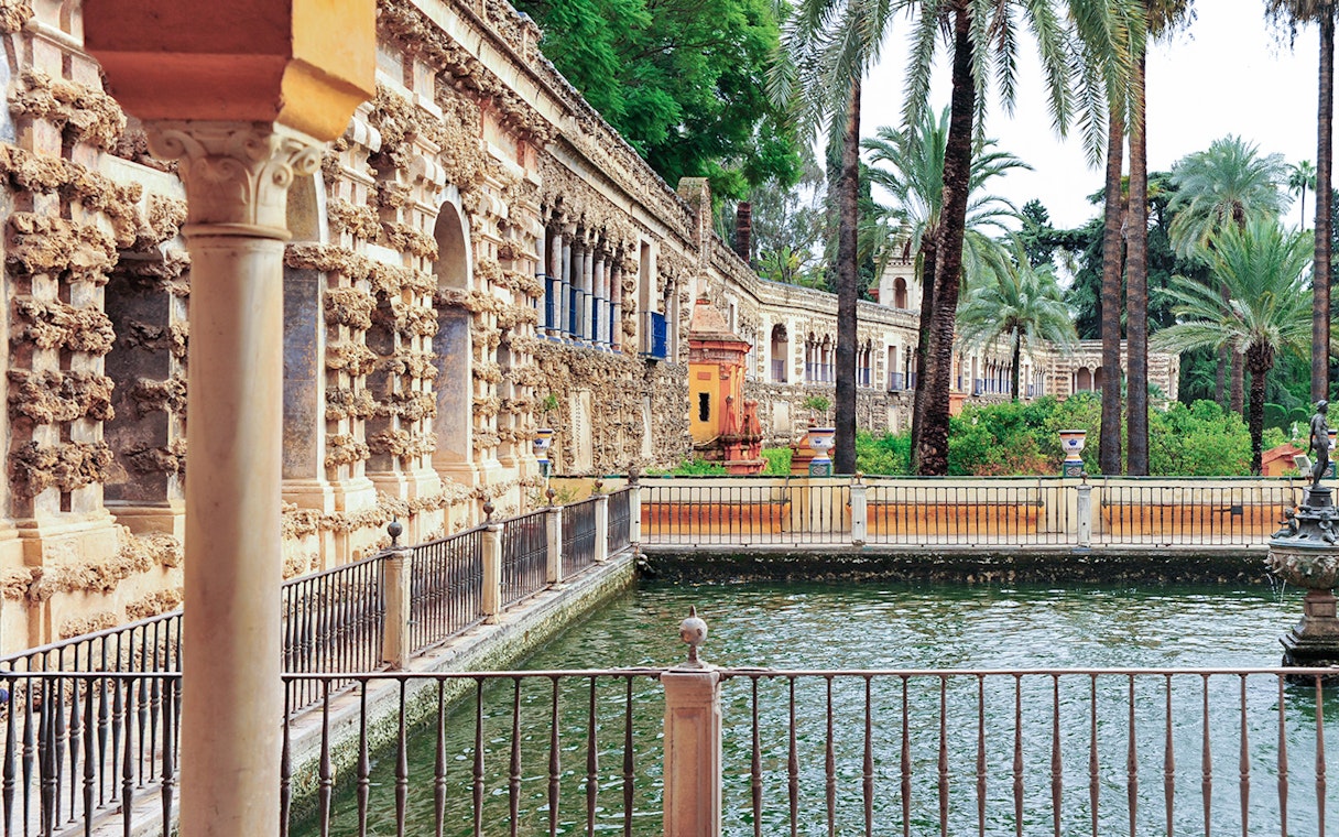 Alcazar of Seville courtyard with ornate architecture and palm trees.