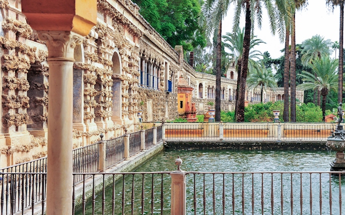 Alcazar of Seville courtyard with ornate architecture and palm trees.