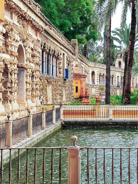 Alcazar of Seville courtyard with ornate architecture and palm trees.