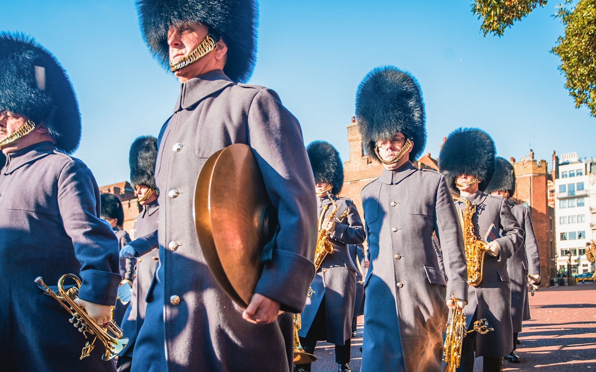 Royal guards in traditional uniforms marching near Tower Bridge, London.