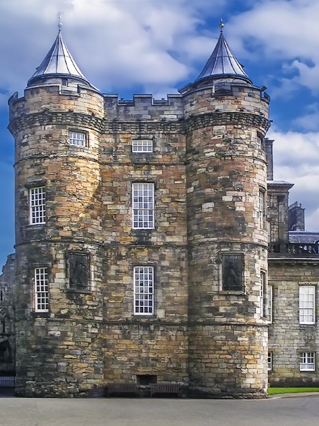 Holyroodhouse Palace facade with stone towers and blue sky in Edinburgh, Scotland.