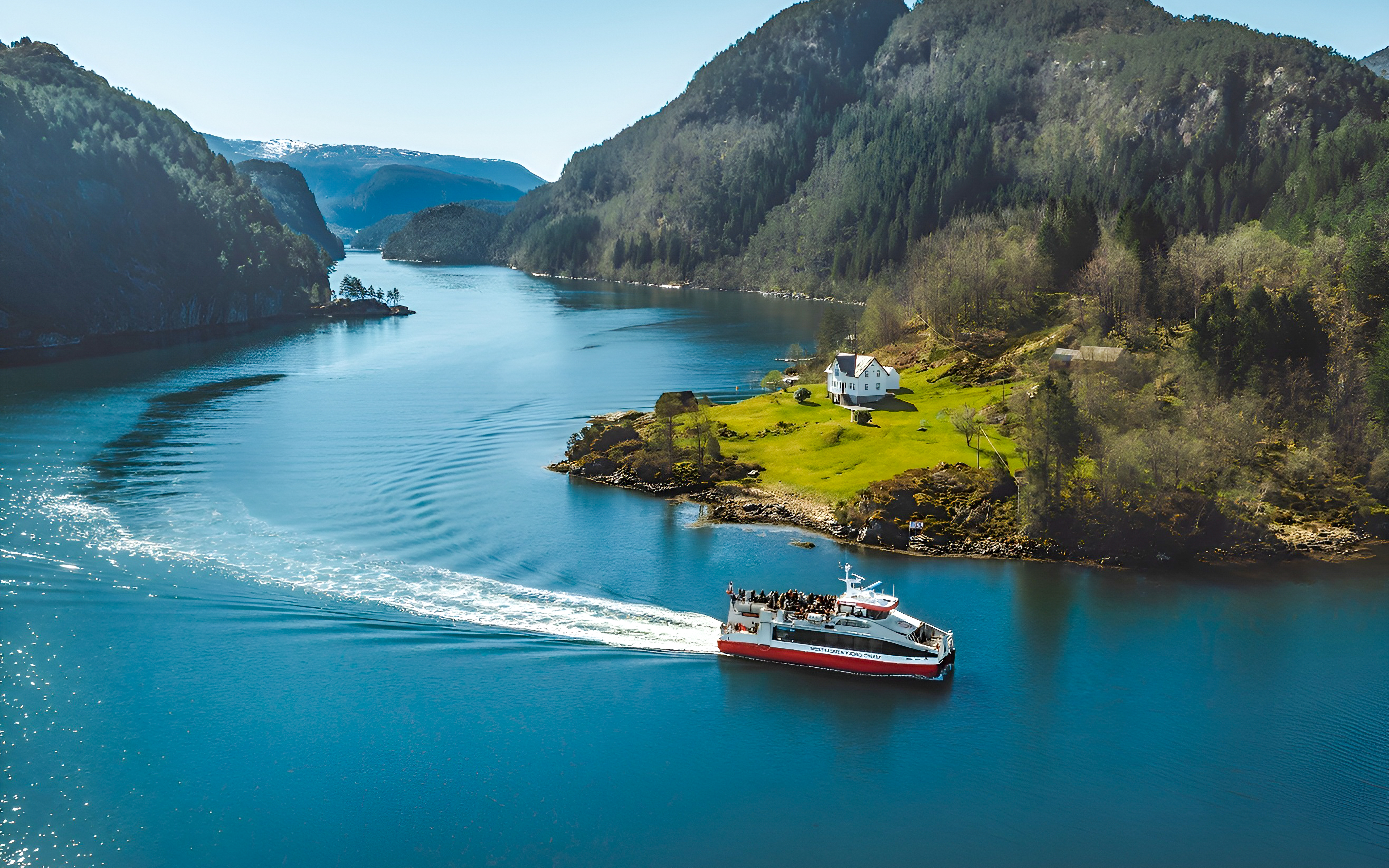 Cruise boat on Mostraumen Fjord near Bergen, passing a scenic green landscape with a white house.