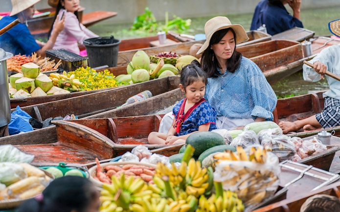 Asian tourists in a boat at a floating market with tropical fruits in Thailand.