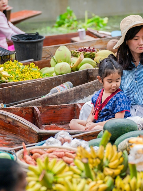 Asian tourists in a boat at a floating market with tropical fruits in Thailand.