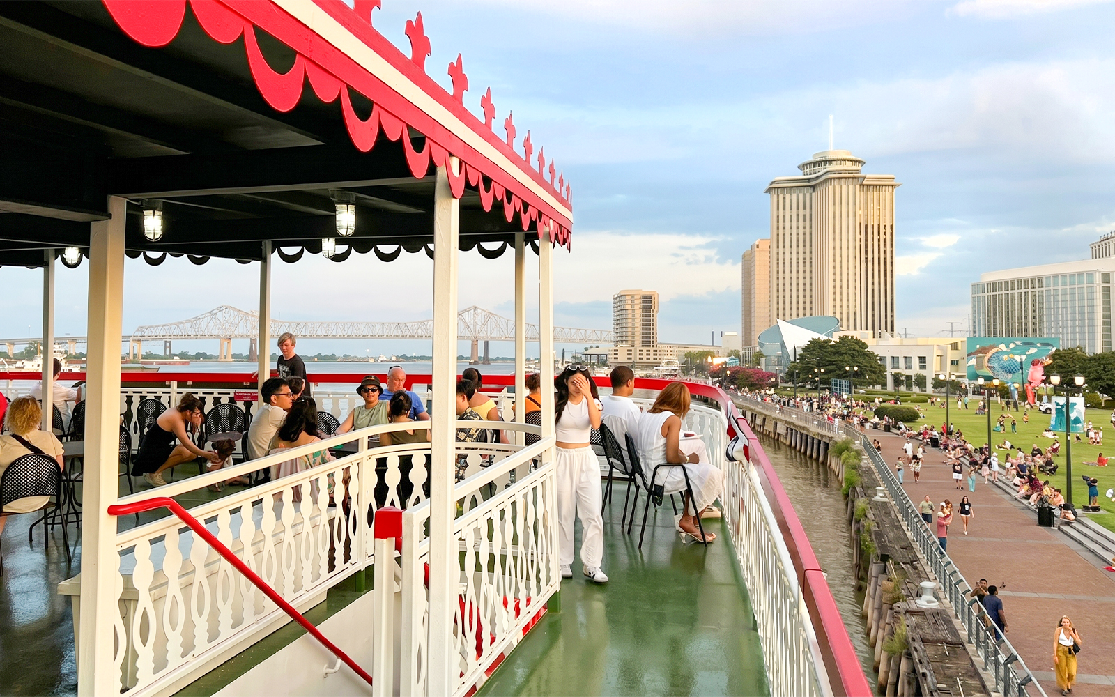 Riverboat cruise passengers enjoy views of New Orleans skyline and Mississippi River bridge.
