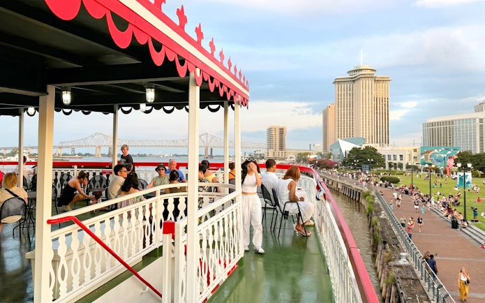 Riverboat cruise passengers enjoy views of New Orleans skyline and Mississippi River bridge.
